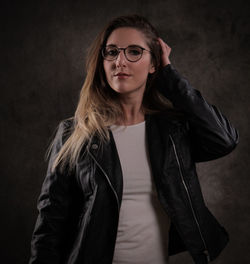 Portrait of young woman standing against black background