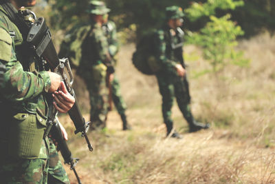 Midsection of army soldier holding gun while standing outdoors