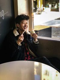 Cheerful young man eating ice cream while sitting by window in store