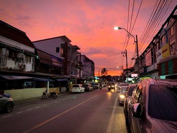 Cars on city street against sky at sunset