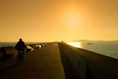 Rear view of silhouette man riding bicycle on pier