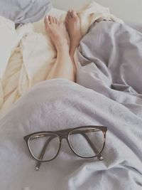 Low section of man lying down with eyeglasses on blanket over bed