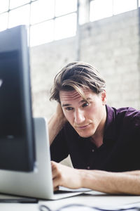 Young male entrepreneur working on start-up project while coding at desk in office