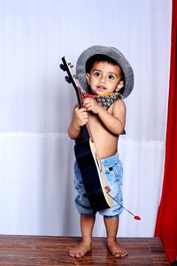 Full length portrait of cute boy standing against wall wearing a hat