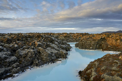 Scenic view of blue lagoon with volcanic shore in cloudy day