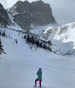 A woman hides her face from the wind as she stares at the rocky mountains