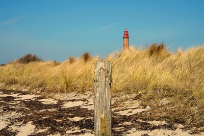 Lighthouse on field by building against sky