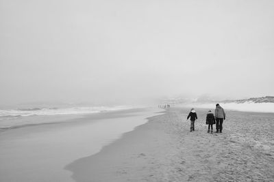 Rear view of people walking on beach wintertime