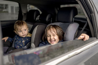 Happy siblings sitting on backseat of car