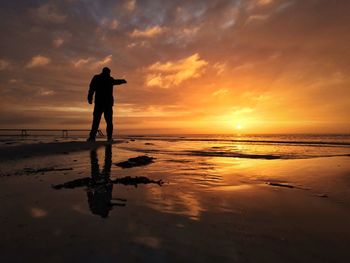 Silhouette man standing at beach against sky during sunset