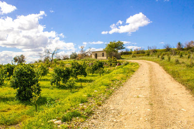 Dirt road amidst field against sky