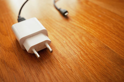 A white smartphone charger lies on the wooden brown floor