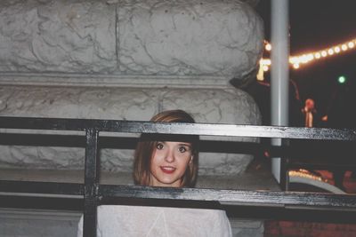 Close-up portrait of young woman seen through railing at night
