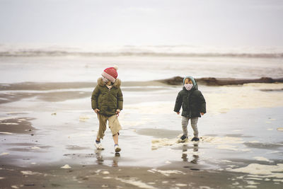 Full length of kids wearing mask walking on beach against sky