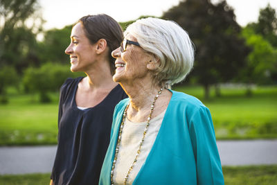 Smiling grandmother looking away while standing by granddaughter at park