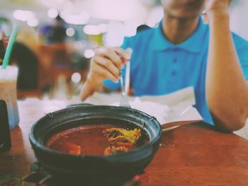 Close-up of asam pedasin bowl on table against man at restaurant