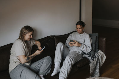 Female couple sitting together on sofa and using cell phones