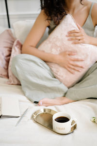 Midsection of woman with coffee cup on bed