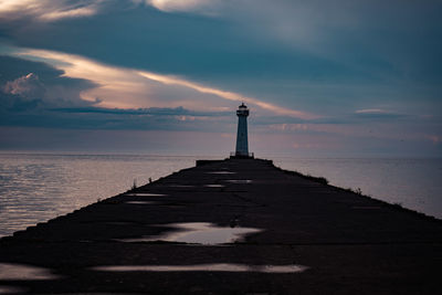 Lighthouse by sea against sky during sunset