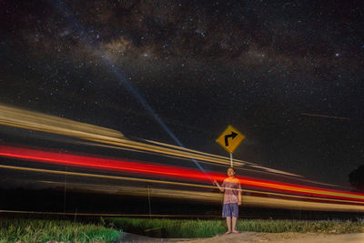 Man holding torch while standing by light trails against star field