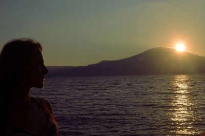 Side view of woman by sea against sky during sunset