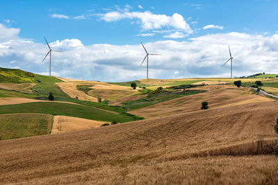 Row of wind turbines in a wind farm on the hilltops viewed across rolling agricultural land