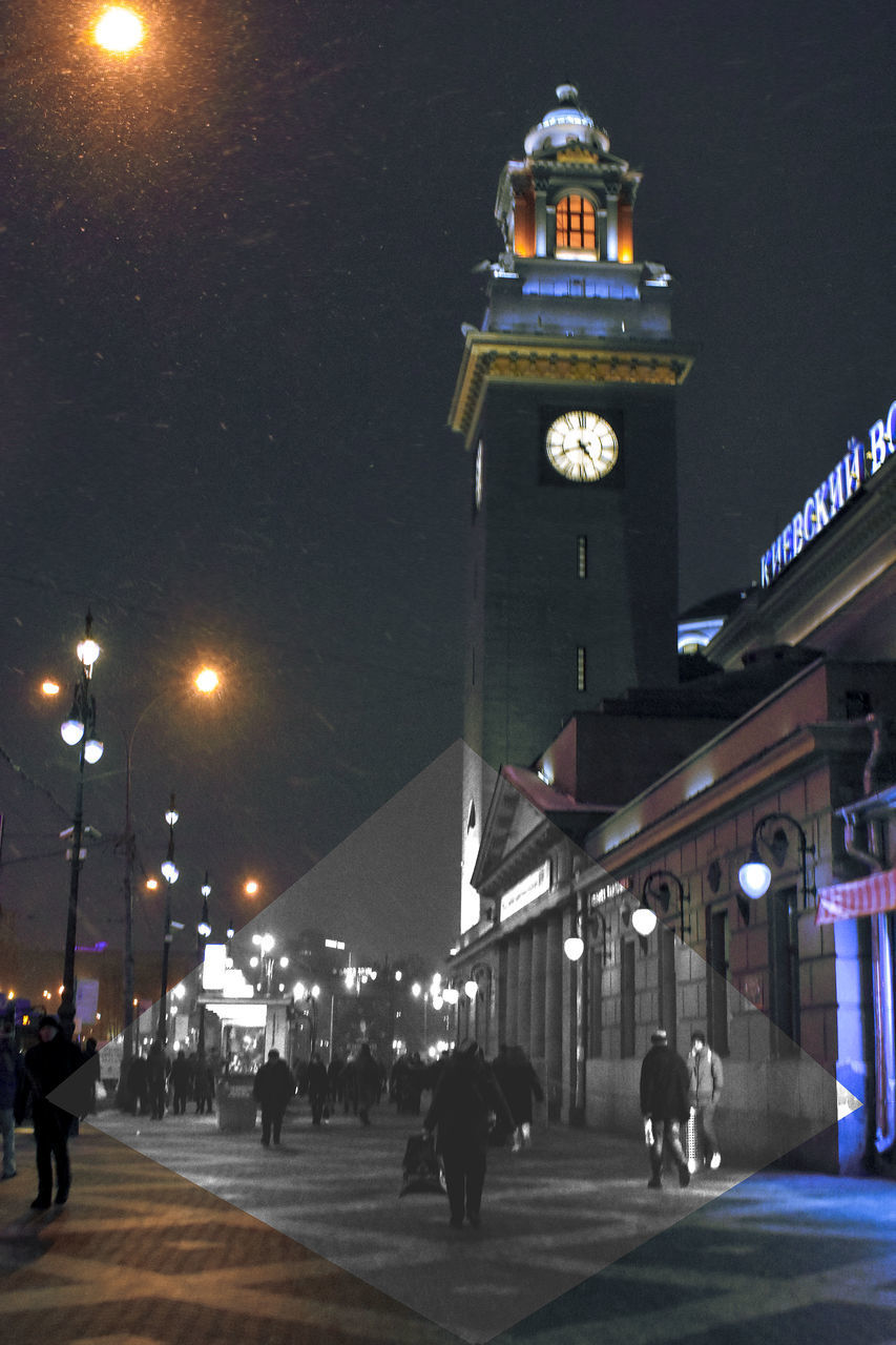 PEOPLE ON ILLUMINATED STREET AMIDST BUILDINGS AT NIGHT