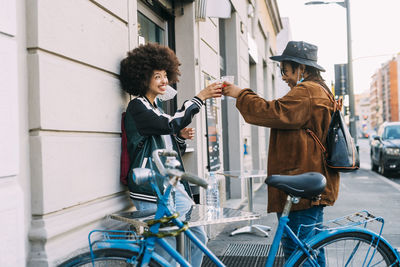 Smiling friends toasting juice while standing by bicycle on footpath