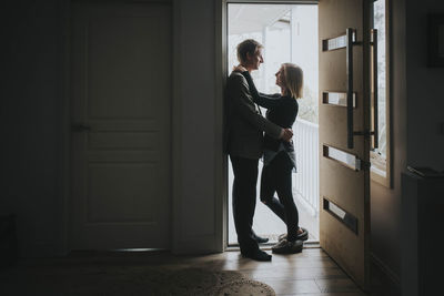 Full length of couple romancing while standing at doorway
