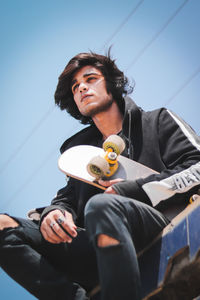 Low angle view of young man looking away while sitting against sky