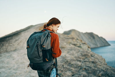 Young woman standing on rock by sea against clear sky