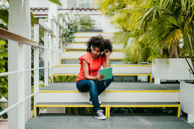 Full length of young woman using phone while sitting on bench