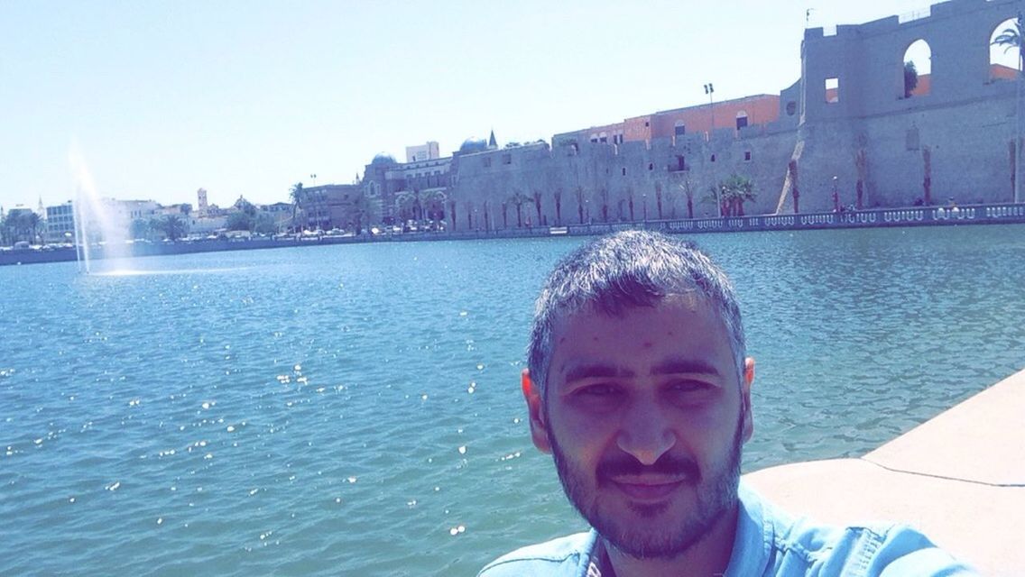 water, architecture, building exterior, built structure, lifestyles, young adult, leisure activity, person, clear sky, young men, portrait, headshot, waterfront, looking at camera, blue, sunlight, city, day