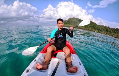 Portrait of smiling young man kayaking in sea against sky