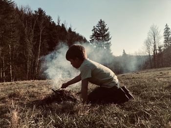 Side view of boy making fire on a field