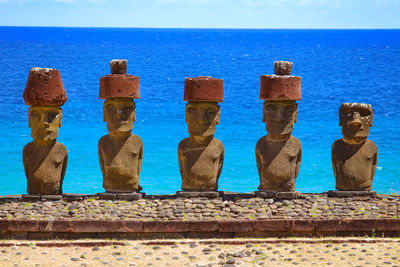 Statues on beach against blue sky