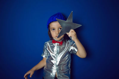 Christmas boy child holding a star in a silver shirt blue hat and red bow tie stands in the studio