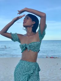 Young woman standing at beach against sky