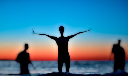 Silhouette people standing by sea against clear sky during sunset