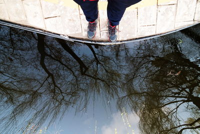 Low section of man standing by lake with trees reflecting