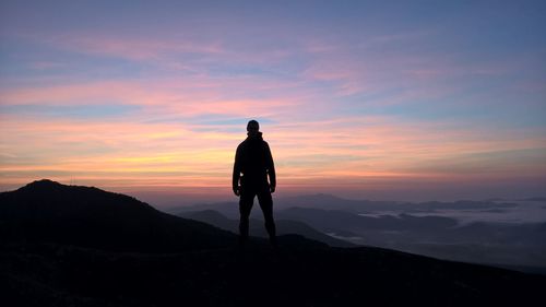 Rear view of silhouette man standing on mountain against sky