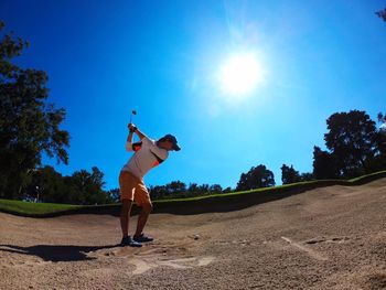 Full length of man playing golf on sand against sky