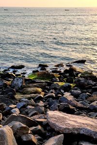 Rocks at beach against sky during sunset