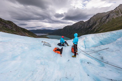 Full length of people on snow cliff against cloudy sky