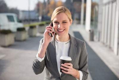 Businesswoman holding coffee while talking on smart phone