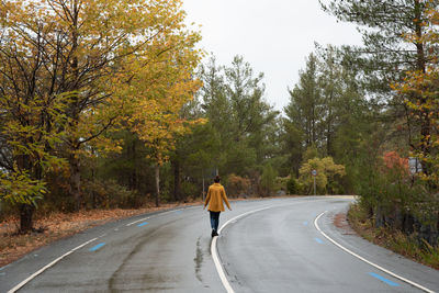 Woman wearing yellow coat walking in the mountain road in autumn.