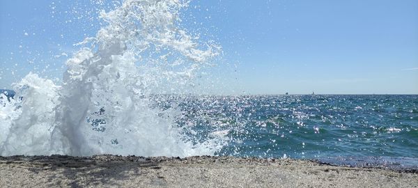 Sea waves splashing on shore against clear sky