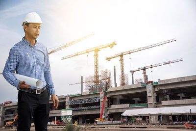 Confident architect with blueprint standing at construction site