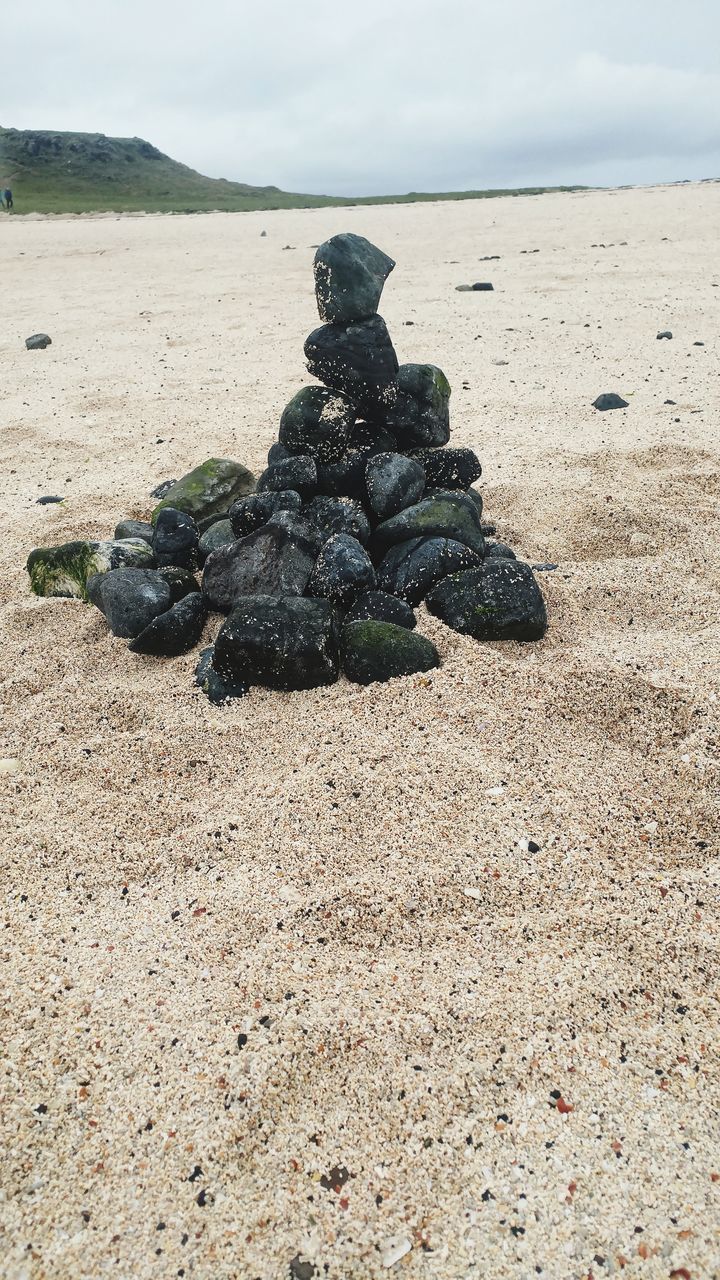 STACK OF PEBBLES ON SAND AT BEACH