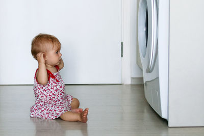 Side view of cute girl sitting by washing machine